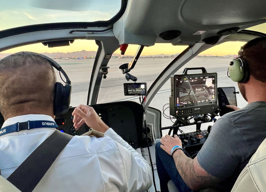 Film crew member operating the SHOTOVER camera control deck inside an EC130 Maverick helicopter during aerial production setup.