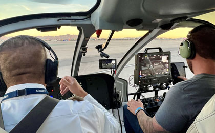 Film crew member operating the SHOTOVER camera control deck inside an EC130 Maverick helicopter during aerial production setup.