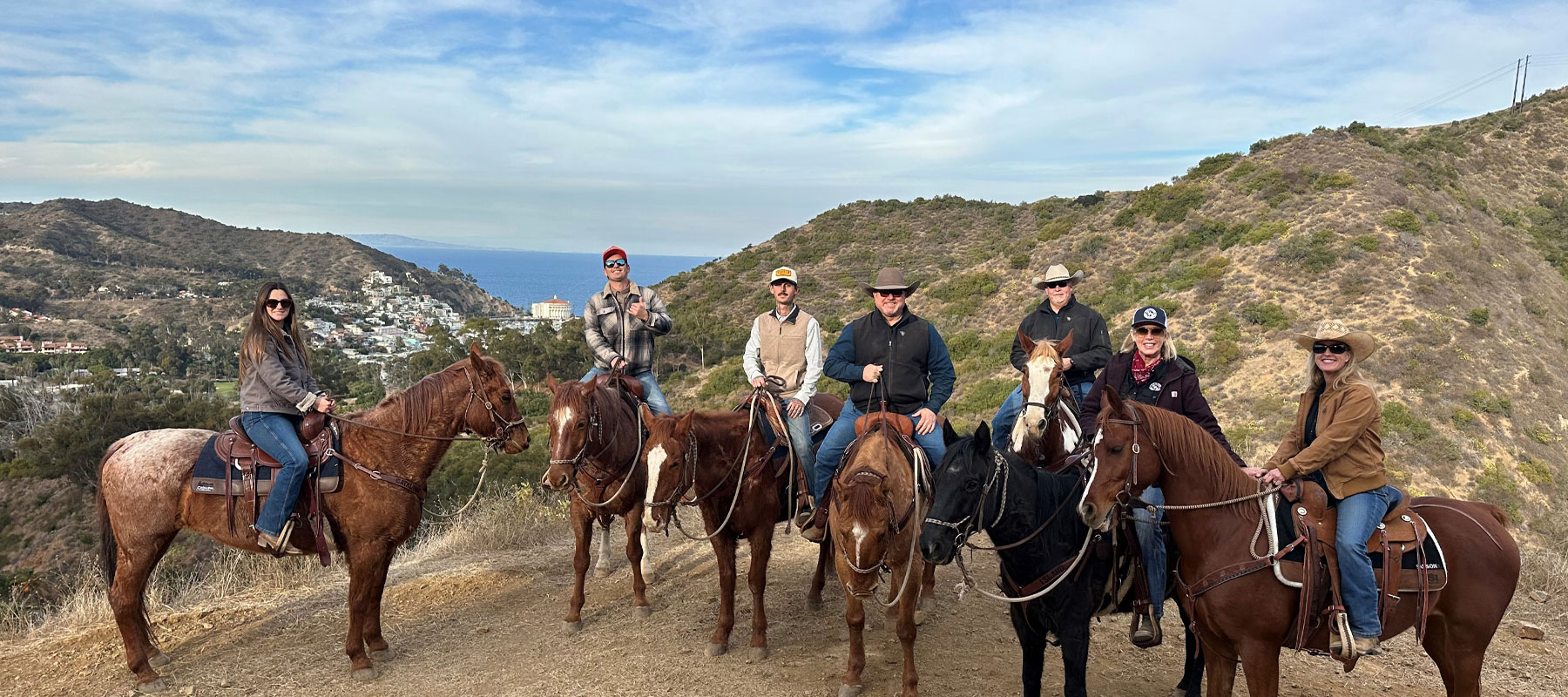 Group of riders lined up on horseback with ocean views behind